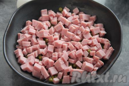 Поверх горошка равномерно разложить ветчину, нарезанную на небольшие кубики.