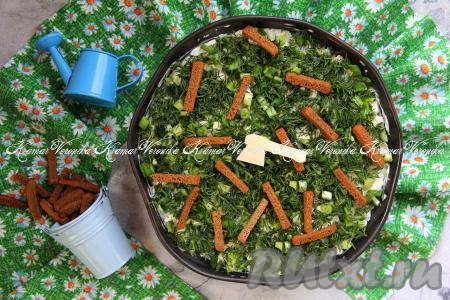 Поверх зелени выложить сухарики и сразу подать яркий, красивый и очень вкусный салат "На траве дрова" к столу.