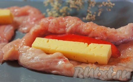 Выложить на каждую куриную отбивную брусочек сыра и кусочек красного перца, затем свернуть плотным рулетом. У нас получатся 2 рулетика с начинкой из сыра и перца.
