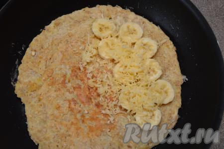 Затем аккуратно перевернуть овсяноблин на другую сторону. Так как овсяноблин большой, он может порваться при переворачивании при помощи лопатки, поэтому я предпочитаю переворачивать его при помощи тарелки. Для этого нужно в одной руке держать за ручку сковороду, в другую руку нужно взять плоскую тарелку, диаметр которой должен быть не меньше диаметра блина. Максимально близко поднести тарелку к блину и одновременно перевернуть сковороду и тарелку. Блин окажется на тарелке. Затем уже с тарелки аккуратно переложить овсяноблин необжаренной стороной вниз на сковороду. На половину блина выложить отложенные кружочки банана и посыпать их оставшимся сыром.