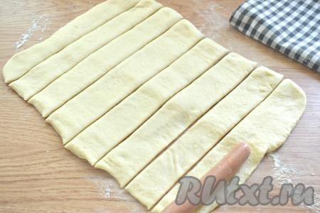 Дрожжевое тесто на столе, присыпанном мукой, раскатываем в прямоугольный пласт, ширина которого должна быть больше длины сосисок в 2 раза. Нарезаем пласт на полоски шириной примерно 2,5-3 сантиметра. Полосок должно быть столько же, сколько сосисок (у меня - 8 штук).