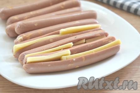 Сыр твёрдых сортов нарезаем на тонкие пластинки и вставляем в разрез каждой сосиски.