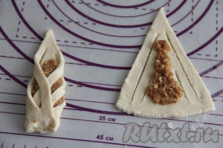 На каждом треугольнике сделать разрезы по бокам. В серединку треугольника выложить немного ореховой начинки, вначале одной стороной треугольника накрыть часть начинки, затем накрыть начинку второй стороной треугольника, как на фото, низ получившегося "башмачка" прищепить. Вот такая интересная заготовка печенья получилась. Аналогично сформировать все 24 заготовки творожного печенья с орехами.