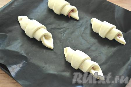 Круассаны с беконом выкладываем "хвостиком" вниз на противень, застеленный специальным листом для выпечки (или пергаментом). Круассаны обязательно выкладывайте на расстоянии друг от друга, так как во время выпечки они увеличиваются в размере.