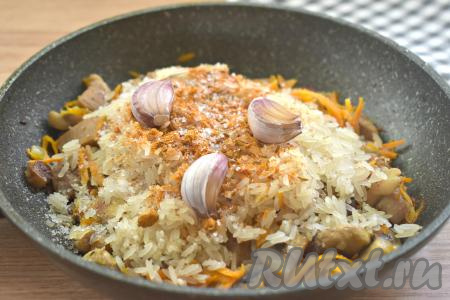 По вкусу солим содержимое сковороды, всыпаем приправу для плова. Зубчика чеснока ополаскиваем водой, убирая только грязную шелуху. Очищать зубчики чеснока не нужно. Добавляем зубчики чеснока в сковороду, аккуратно разравниваем.