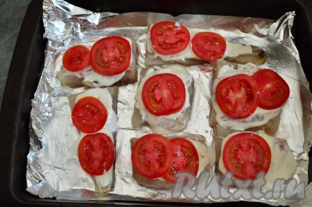 Острым ножом помидоры нарезать на тонкие кружочки. Выложить кружочки помидоров на каждый кусочек рыбки и присолить. Отправить форму с рыбой запекаться в разогретую до 180 градусов духовку на 15 минут.