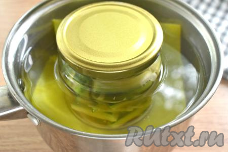 Банку прикрываем заранее прокипячённой крышкой. На дно кастрюли выкладываем полотенце (или тканевую салфетку, сложенную в 2 раза), ставим банку с огурцами. Вливаем в кастрюлю столько тёплой воды, чтобы она доходила до "плечиков" банки с огурчиками, ставим на средний огонь. После закипания, уменьшив огонь, стерилизуем банку с огурцами по-корейски 15 минут.