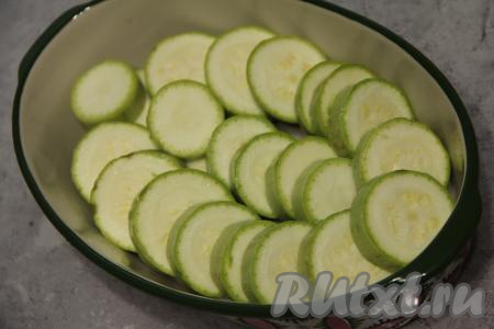 Кабачок нарезать на кружочки толщиной 1,5 сантиметра, выложить их внахлёст в жаропрочную форму, заранее смазанную маслом.