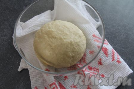 Подсыпая постепенно оставшуюся просеянную муку, перемешивать дрожжевое тесто вначале ложкой. А когда тесто начнёт собираться в ком, продолжать выполнять замес руками, добавляя понемногу муку. Вымешивать тесто руками нужно не менее 7-8 минут. Добавляя муку в процессе замешивания теста, учитывайте, что тесто должно получиться мягким, податливым и не липнуть к рукам. Собрать замешанное дрожжевое тесто в шар. Накрыть миску с тестом полотенцем и на 1 час поставить в тёплое место.