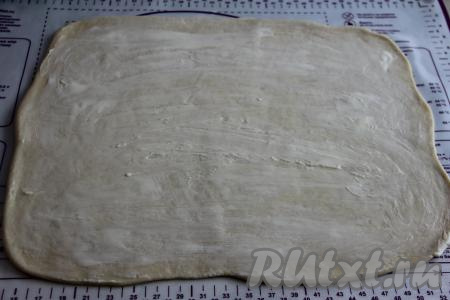 Обмять тесто, а затем раскатать его на присыпанную мукой поверхность в прямоугольный пласт, его толщина должна быть примерно 3 миллиметра. Смазать пласт 50 граммами мягкого сливочного масла.