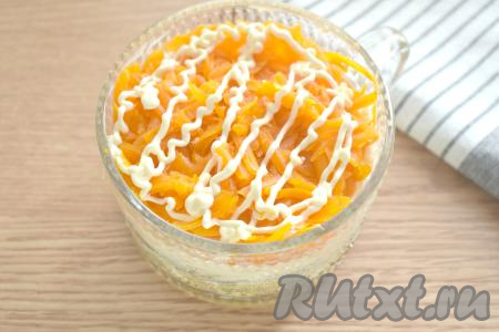 Следующим слоем выкладываем натёртую на крупной тёрке морковку, смазываем немного майонезом.