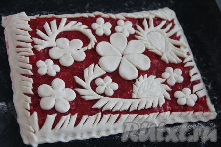 Вторую часть слоёного теста будем использовать для украшения пирога. Для этого тесто нужно немного раскатать, затем вырезать 4 полоски теста (длина полосок должна быть равна длине сторон прямоугольника, на который выложена ягодная начинка), надрезать эти полоски с одной стороны (получится что-то наподобие веточек), выложить по краям пласта теста с начинкой и хорошо скрепить края пирога. Затем вырезать из оставшегося теста цветочки или любые украшения (я вырезала с помощью вырубки для мастики) и разместить их поверх начинки пирога.