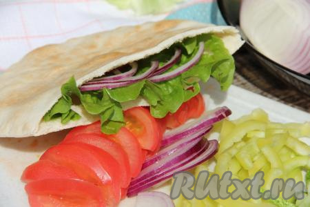 В кармашек, открывшийся в пите, выложить лист салата, немного помидоров, перца, огурцов, лука и куриного мяса. Заполнить весь кармашек питы начинкой.