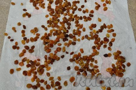 Изюм выложить в сито, промыть проточной водой, затем переложить в небольшую ёмкость, залить полностью кипятком и оставить минут на 5. Откинуть изюм на сито, чтобы стекла вода, в которой он замачивался, а после этого обсушить его, выложив на бумажное (или тканевое) полотенце. После того как разложите изюм на полотенце, осмотрите изюминки, чтобы они были без веточек. Если веточки есть, их нужно будет удалить.