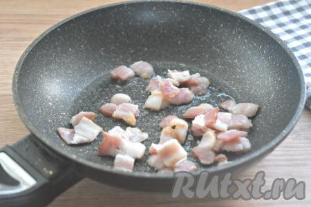 Шампиньоны моем, даём им немного обсохнуть. Разогреваем на сковороде растительное масло. Полоски бекона нарезаем на небольшие кусочки, выкладываем в горячее масло на сковороду и, периодически перемешивая, обжариваем 2 минуты на среднем огне.