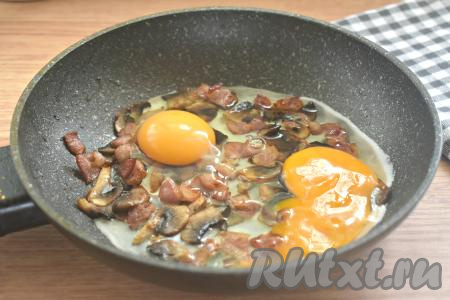 Разбиваем к грибам и бекону яйца.