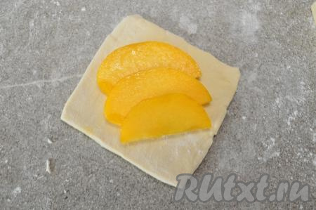 На каждую квадратную заготовку из слоёного теста выложить в центр по 3 кусочка персика внахлёст.