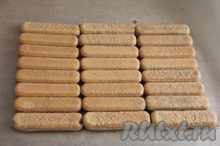 Я решила сформировать десерт "Тирамису" в виде рулета. Для этого стол нужно застелить пергаментом. Полностью окунуть каждое печенье "Савоярди" в кофе и выложить на пергамент в один слой, как на фото.