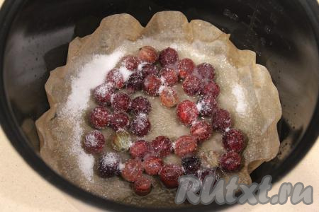 Дно чаши мультиварки застелить пергаментом. Выложить подготовленный крыжовник в один слой, присыпать ягоды 1 столовой ложкой сахара.