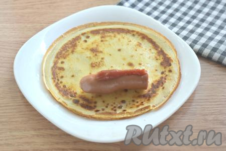 С сосисок снимаем слюду. А затем отвариваем сосиски в течение 2 минут с момента закипания воды (или подрумяниваем со всех сторон на сковороде). У меня были длинные сосиски, поэтому я разрезала их пополам. Если вы взяли маленькие сосиски, тогда их нужно выкладывать на блины целиком, но тогда сосисок потребуется штук 15. На готовый блинчик ближе к одному краю выкладываем половину (или целую) подготовленную сосиску. Сверху смазываем сосиску томатным соусом (или кетчупом).