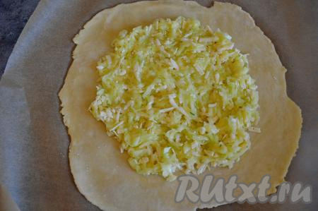 Достать тесто из холодильника. Застелить стол пергаментом и прямо на пергаменте раскатать тесто в круг толщиной примерно 2-3 миллиметра. В центр раскатанного круга, отступив от краёв по 3-4 сантиметра, равномерно выложить кабачково-сырную массу.