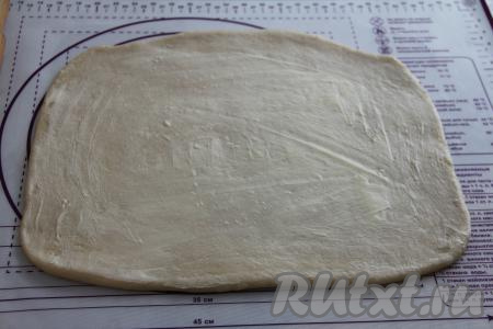 Выложить поднявшееся тесто на присыпанную мукой рабочую поверхность и раскатать скалкой в пласт толщиной ориентировочно 3 миллиметра. Щедро смазать тесто сливочным маслом комнатной температуры.