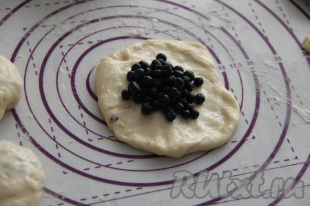 По прошествии времени разделить тесто на 10 частей. Из каждой части теста на припылённой мукой рабочей поверхности сформировать руками круглую лепёшку. Чтобы легче было работать с тестом, руки можно смазать растительным маслом. Выложить в центр лепёшки 2 чайных ложки черники.