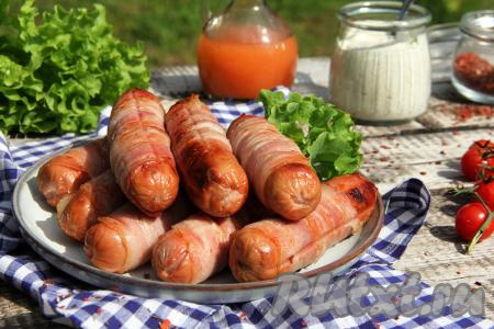 Аппетитные, сочные, ароматные сосиски в беконе переложить с решётки мангала на тарелку и подать к столу, дополнив соусом, лавашом или гарниром.