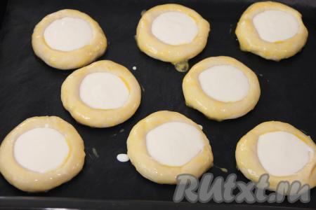 Яичный желток взбить в небольшой ёмкости с помощью вилки до однородности. Края ватрушек смазать взбитым желтком.