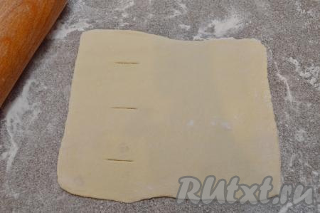 Взять одну заготовку из слоёного теста и на присыпанном мукой столе раскатать её в прямоугольник толщиной примерно 2 миллиметра (размер получился 16 на 19 сантиметров). Ближе к одной стороне прямоугольника сделать три небольших надреза ножом.