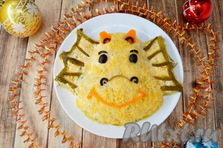 Крылья дракончика сформировать из тонко нарезанных кусочков маринованного огурца, глаза и бровки - из чёрных маслин. Рожки вырезать из отварной морковки и украсить маслинами, носик сделать из маслин и кусочка огурчика, рот - из отварной морковки. Салат сразу можно подавать к новогоднему столу.