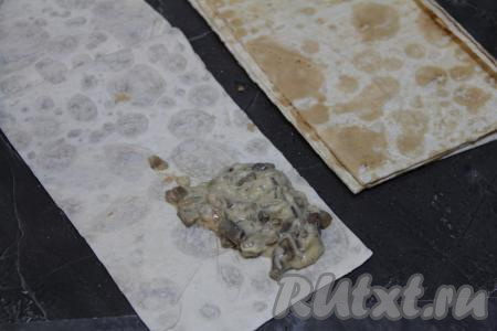 Лаваш нарезать на полоски размером 10 сантиметров на 25 сантиметров. На край полоски из лаваша выложить 2 столовых ложки начинки, как на фото. Завернуть вначале на начинку чистый уголок лаваша, находящийся рядом с начинкой, в виде треугольника, затем продолжить складывать лаваш с грибной начинкой в виде треугольника.