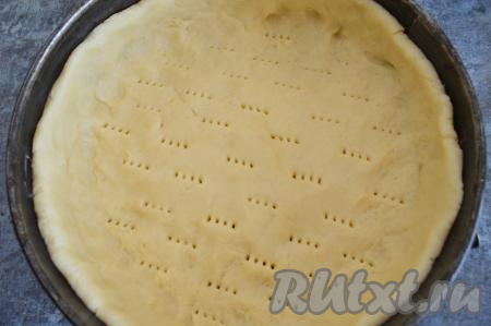 По прошествии времени достать песочное тесто из холодильника. Дно и бока формы для выпечки (у меня разъёмная форма диаметром 22 сантиметра) смазать небольшим кусочком сливочного масла. Тесто равномерно распределить по дну форму, формируя бортики. По дну формы на тесте вилкой сделать проколы. Проколы нужны, чтобы песочное тесто сильно не поднималось во время выпечки в духовке.