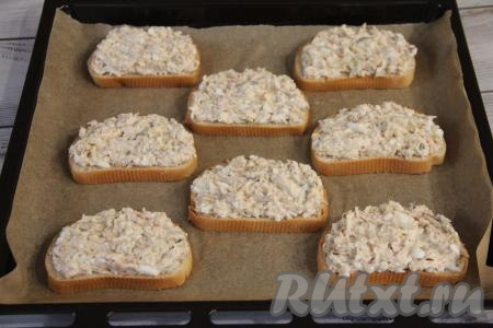 Выложить ломтики батона на противень, застеленный пергаментом для выпечки. Равномерно разложить рыбно-сырную массу поверх хлеба.