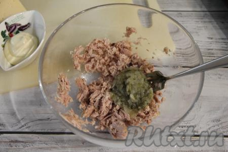 Открыть банку с консервированным тунцом, слить лишнюю жидкость, рыбку переложить в миску. Размять тунца в миске вилкой. В отдельную ёмкость натереть маринованный огурец на мелкой тёрке, затем отжать с него лишний сок. Огурец, отжатый от лишней жидкости, добавить в миску с размятым тунцом.