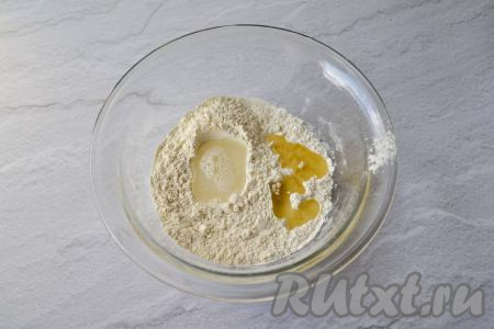 Влейте растительное масло и начните понемногу вливать тёплую воду (температура вода должна быть не выше 40 градусов), перемешивая тесто вначале ложкой.