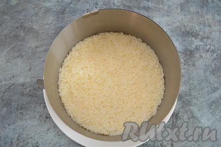 Рис отварить заранее до готовности, промыть и остудить. Морковь в кожуре и яйца тоже отварить до готовности. Дать варёным моркови и яйцам полностью остыть, затем очистить. Теперь можно приступать к формированию салата "Мимоза". Для этого формовочное кольцо диаметром 20 сантиметров нужно поставить на плоскую тарелку, выложить подготовленный рис, утрамбовать.