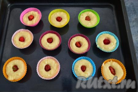 В середину каждого кекса вставить и немного утопить 1 клубнику среднего размера. Если ягоды у вас крупные, тогда разрежьте их пополам и выложите на тесто половинку клубники. Если ягодки мелкие, то выложите поверх теста 2-3 клубнички.