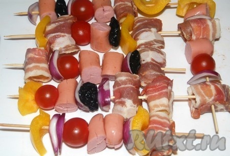 Кусочки сыра обернуть в бекон. Нанизать продукты в любой последовательности на деревянные шпажки.