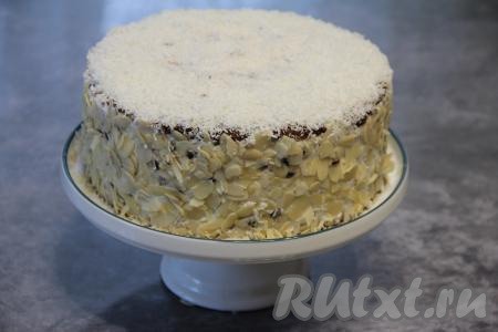 Накрыть второй частью бисквита, пропитать, смазать частью крема. Накрыть третьей частью бисквита. Покрыть торт тонким слоем крема со всех сторон и убрать в холодильник на ночь. Затем бока готового торта обсыпать лепестками миндаля, а верх посыпать кокосовой стружкой.