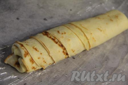 Свернуть блины с начинкой в плотный рулет, начиная с широкой стороны полоски из блинов.