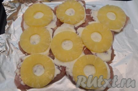 На каждую отбивную выложить кольцо ананаса. Если у вас ананасы кусочками, тогда нарежьте их до толщины 5 миллиметров и просто разложите на отбивные. У меня кольца ананаса были не толстые (толщиной примерно 4-5 миллиметров), поэтому я просто выложила их поверх мяса. Если же у вас кольца ананаса толще 5-6 миллиметров, тогда их лучше нарезать на кусочки толщиной 5 миллиметров и выложить на мясо. Если выложить на мясо толстые кольца ананасов, то в готовом блюде вы не получите объединения вкусов курицы и фруктов. Да и вам просто может не хватить колец для раскладывания поверх каждой отбивной.