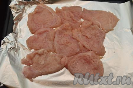 Противень застелить фольгой, затем выложить вплотную к друг другу (не внахлёст) отбитые кусочки куриного филе. Посолить отбивные по вкусу (я каждую отбивную посыпаю щедрой щепоткой соли).