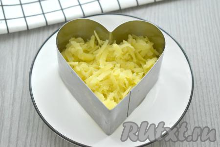 Каждую сервировочную форму ставим на плоскую тарелку. Первым слоем по двум формам раскладываем картофель, натёртый на крупной тёрке.