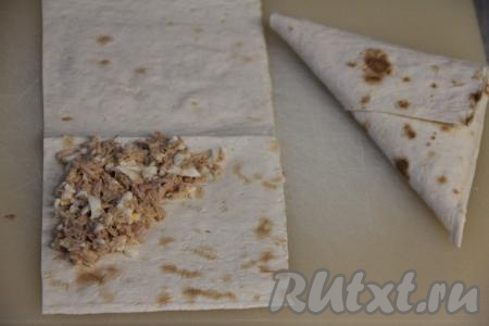 Лаваш нарезать на полоски размером примерно 10 сантиметров на 25 сантиметров. Выложить 1,5 столовых ложки рыбно-яичной начинки на лаваш в форме треугольника (как на фото).