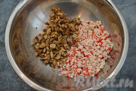 Заранее сварить вкрутую яйца (с момента закипания воды варить 10 минут), после этого полностью их остудить и очистить. Крабовые палочки полностью разморозить при комнатной температуре, затем вынуть их из упаковки. 2 крабовых палочки отложить для украшения. А оставшиеся крабовые палочки нарезать на мелкие кубики, выложить в миску. Консервированные шампиньоны откинуть на сито, чтобы стекла лишняя жидкость, а затем грибы тоже нарезать на мелкие кубики и добавить в миску с крабовыми палочками.