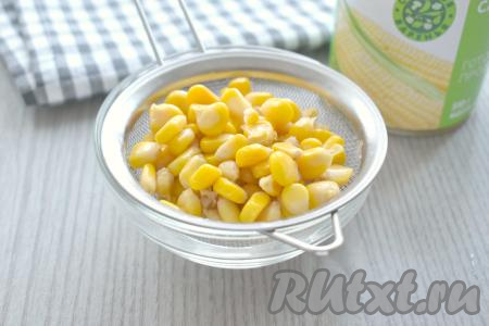Консервированную кукурузу достаём из банки, выкладываем на сито, чтобы слить жидкость с зёрен.