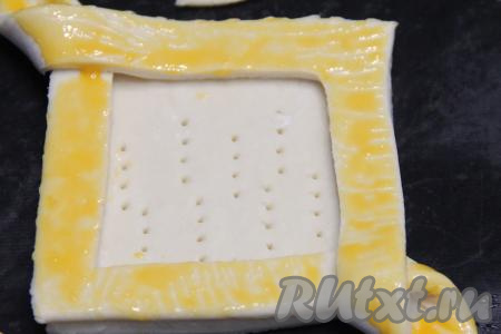 Сырой яичный желток в небольшой ёмкости взбить до однородности. Края слоек смазать взбитым желтком.