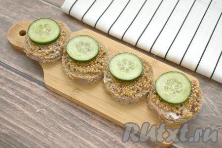 Огурец моем, обсушиваем, нарезаем на тонкие кружочки. По кружочку огурца выкладываем на бутерброды поверх зернистой горчицы. Огурец нужно выкладывать ближе к одному из краёв хлеба, чтобы на хлебе оставалось немного свободного места, на которое в дальнейшем будет выкладываться селёдка.
