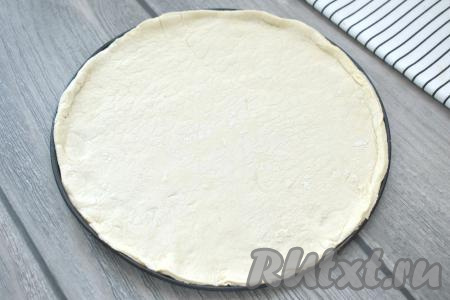 Размороженное тесто на присыпанной мукой поверхности раскатываем в пласт толщиной 3 миллиметра. Основу для пиццы я вырезаю с помощью дна от разъёмный формы для выпечки диаметром 25 см (можно вырезать основу для пиццы и с помощью большой крышки или тарелки). Это же дно формы для выпечки я использую в качестве противня, смазав его немного растительным маслом. 
